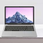 Sleek laptop on a minimalist desk with mountain wallpaper on screen, next to a teapot and cup