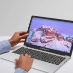 Person using a laptop showing a snowy mountain on the screen, highlighting sleek design and vibrant display